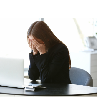 Women with face in her hands looking down with a computer in front of her.